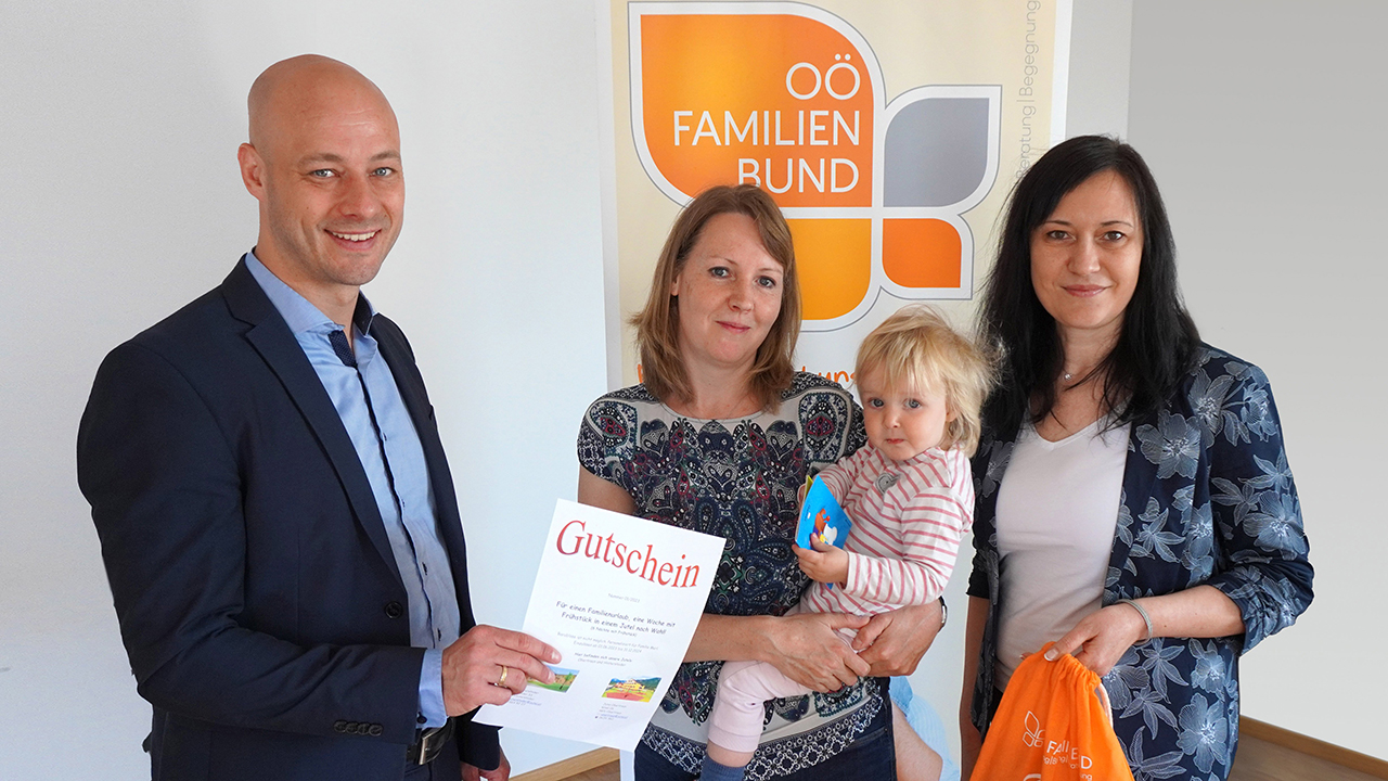 Mama mit Kind bekommen den Urlaubsgutschein in die Hand gedrückt von Martin Hajart