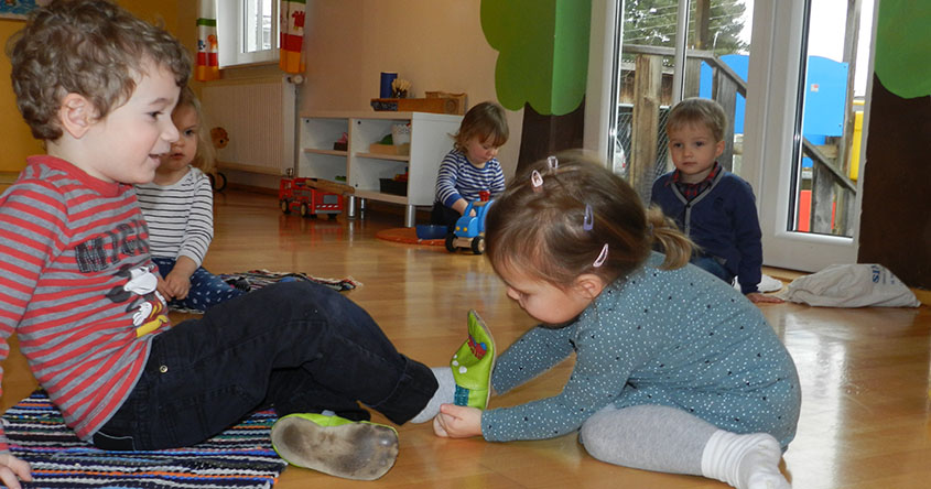 2 Kinder sitzen am Boden. eines zeiht dem anderen den Patschen an