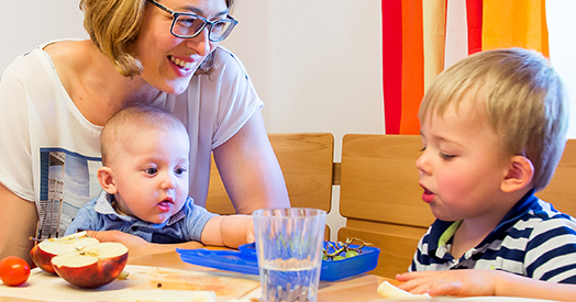 Mama mit Baby und Kinder sitzen am Frühstückstisch